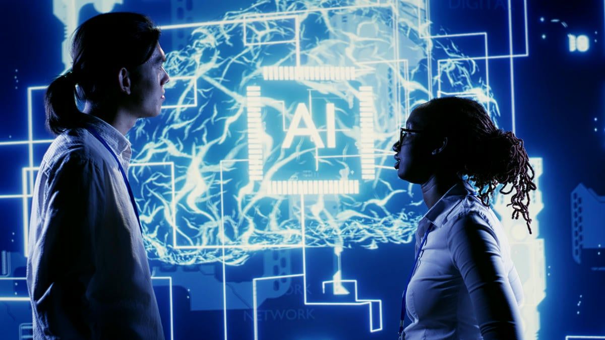 The image shows two individuals standing in front of a large screen displaying an AI interface, symbolizing the use of artificial intelligence in computing and data analysis.