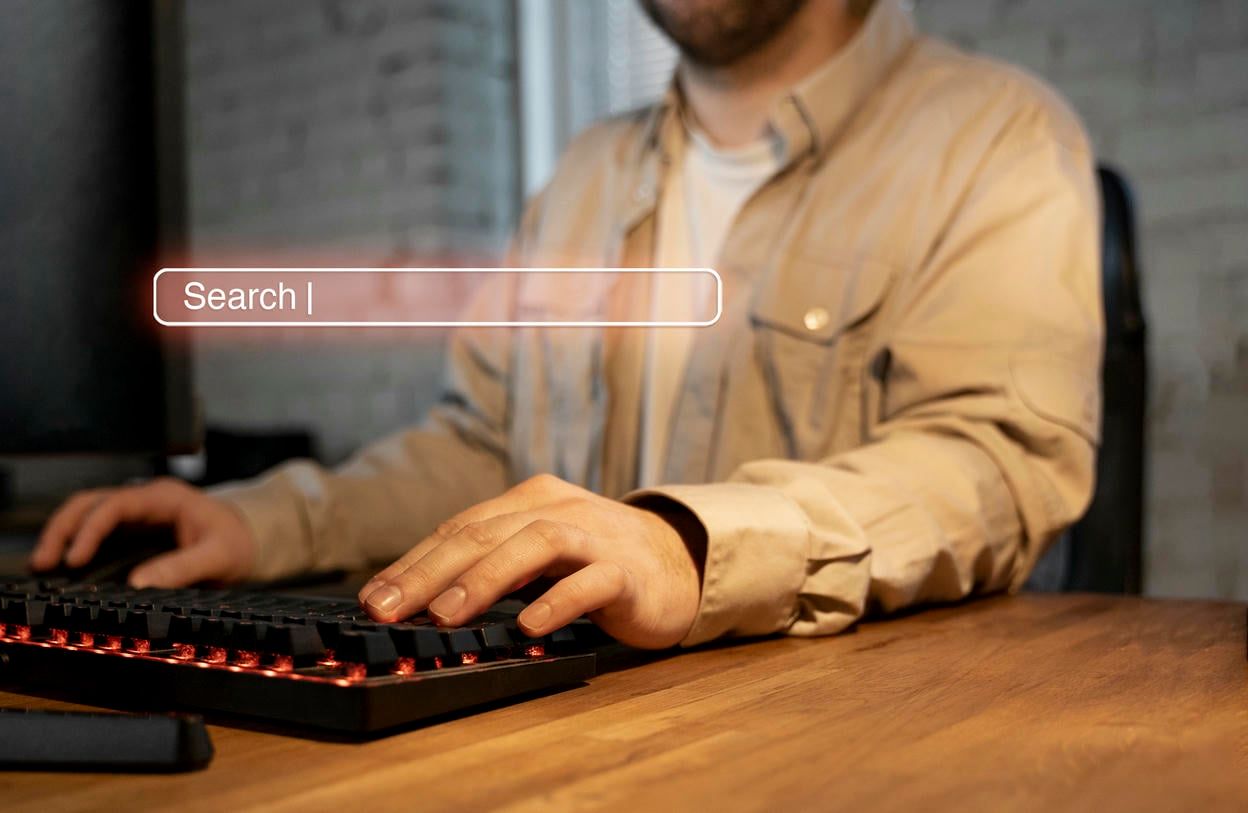 The image shows a person using a backlit mechanical keyboard, with a digital "Search" bar graphic overlaying the scene, symbolizing online searching or digital interaction.