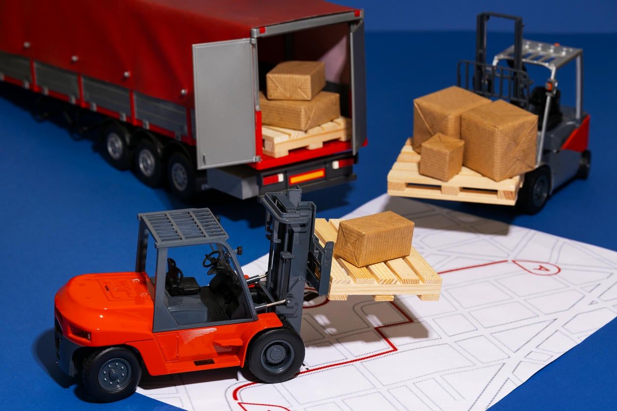 This image is a model representation of a logistics operation, featuring toy forklifts and a truck loading or unloading wooden crates.