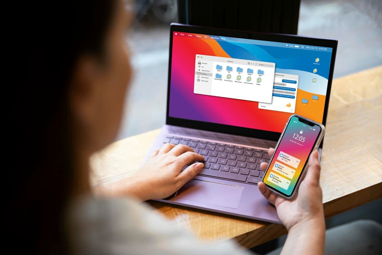 The image captures a woman using a laptop and smartphone simultaneously, showcasing a setup where she is likely managing or synchronizing tasks across both devices.
