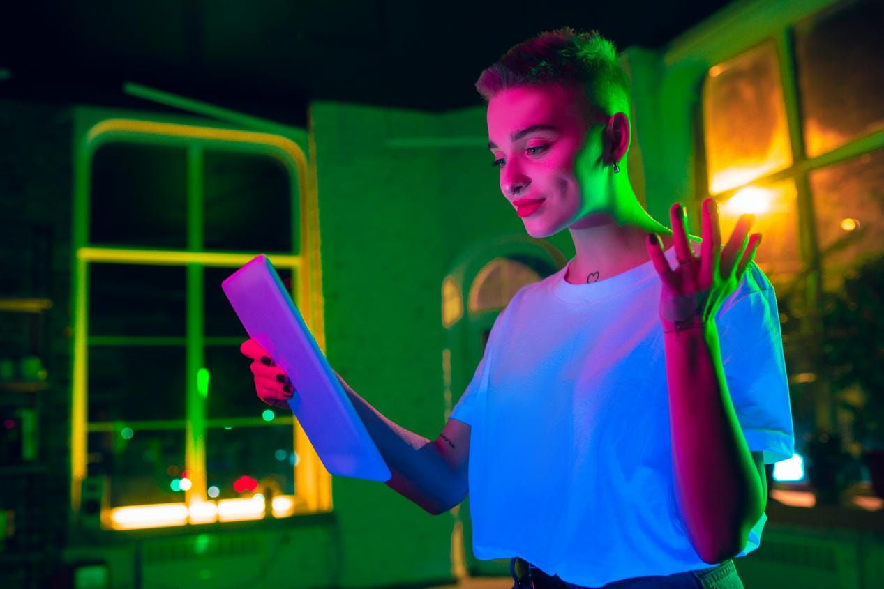 Caucasian model using tablet in colorful lights indoors.