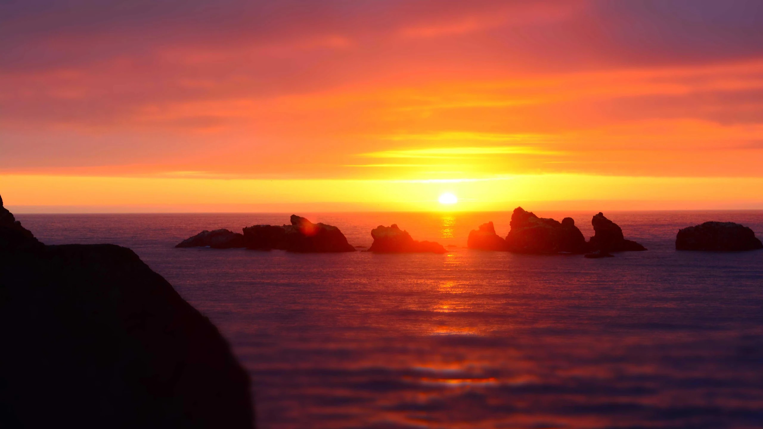 The sun setting over the sea behind dark rocks