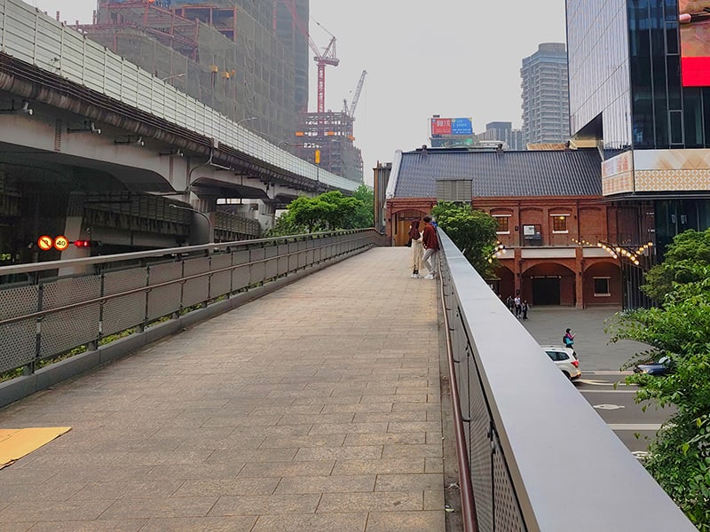 位於臺北車站前的天橋，後方紅磚建物是修復後的歷史建物。天橋上有遊客在此拍照，左後方則是興建中的台北雙子星大樓。在《傷心的歌》MV中還能看到原有的台汽客運站，天橋的樣貌也與現在不同。(圖/張復嘉攝影)