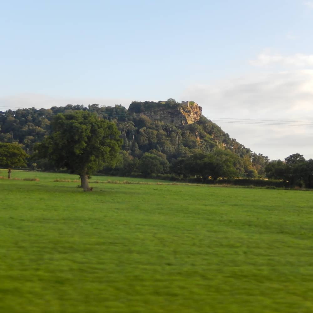 A castle on top of a wooded hill with green fields around