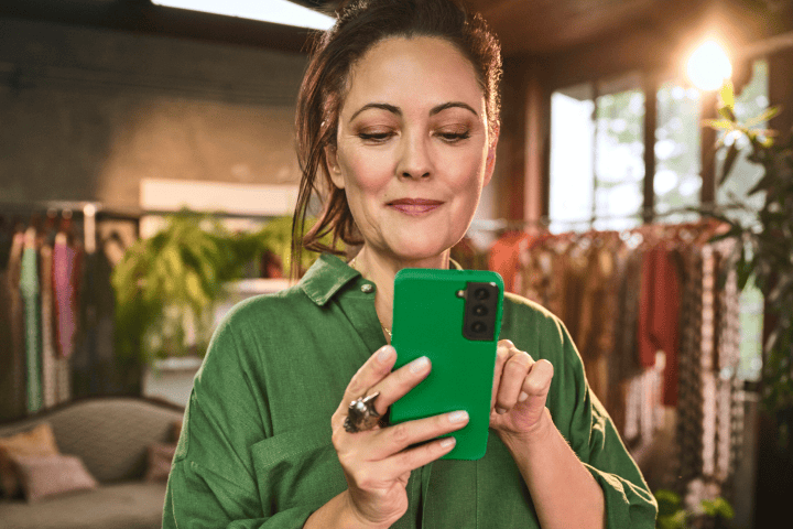 Empreendedora em sua loja de roupa segurando o seu celular