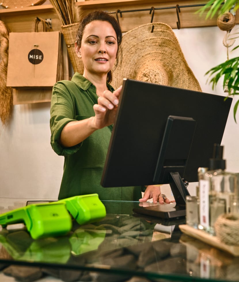 empreendedora na sua loja utilizando o computador com os sistemas integrados da stone e em cima da mesa duas maquininhas de cartão stone