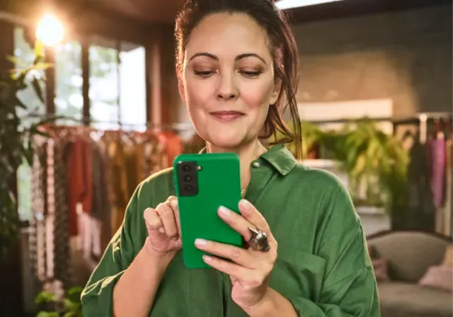 Empreendedora segurando o celular em sua loja de roupas