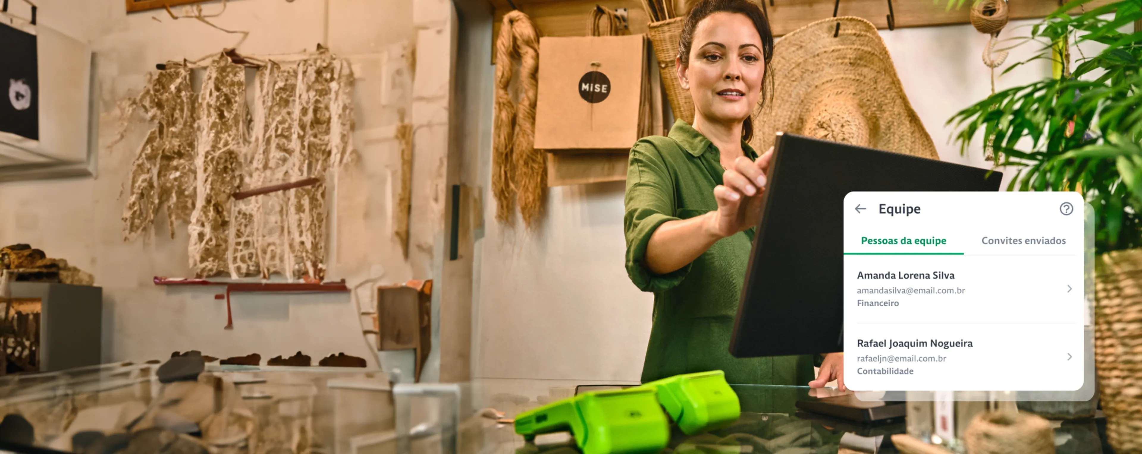 Empreendedora em sua loja utilizando o computador, 2 Maquininhas de Cartão da Stone em cima do balcão e um destaque com o nome e e-mail da equipe.  