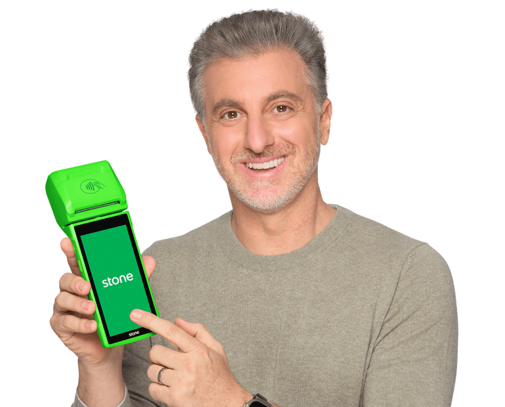 Luciano Huck sorrindo, apresentando uma máquina de cartão verde da Stone.