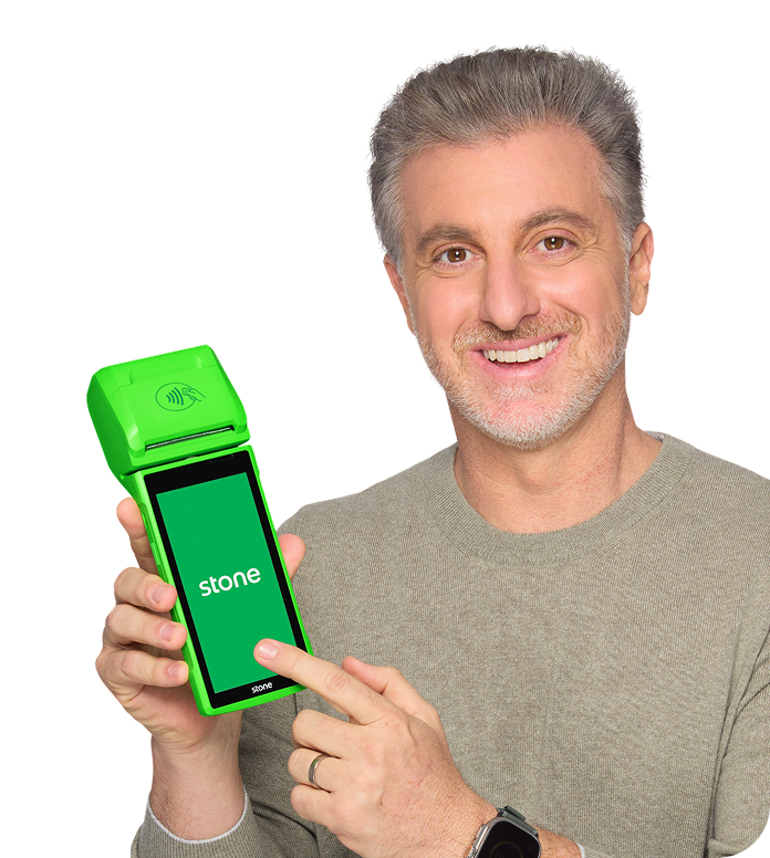 Luciano Huck sorrindo, apresentando uma máquina de cartão verde da Stone. mobile