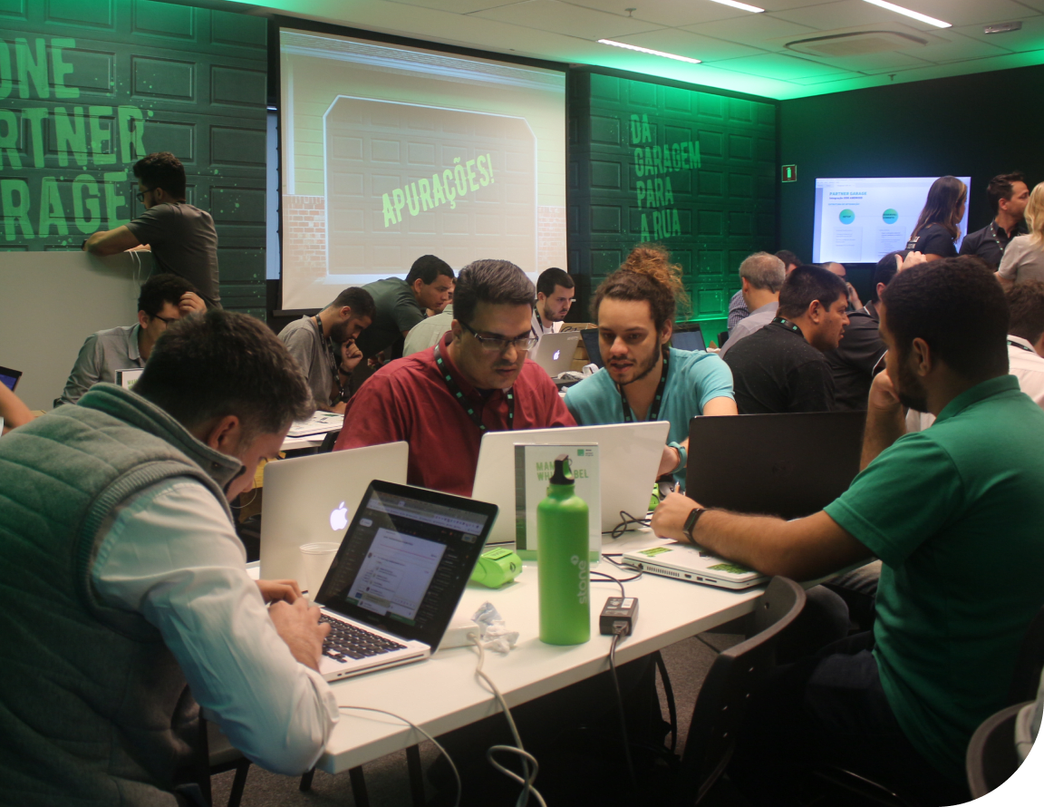 Reunião de diversos colaboradores Stone com seus notebooks reunidos em mesas debatendo as tecnologias