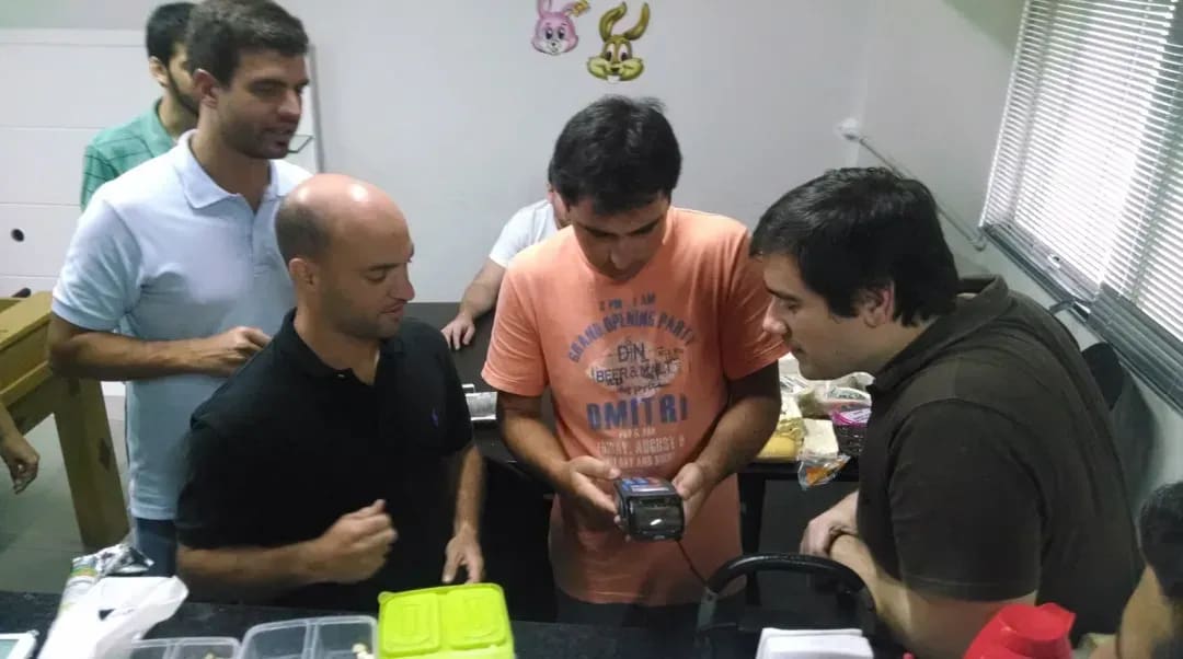 4 homens na imagem e o Mineiro, vendedor de queijos segurando a  maquininha de cartão Stone para ser realizada a sua primeira transação em 2014. 