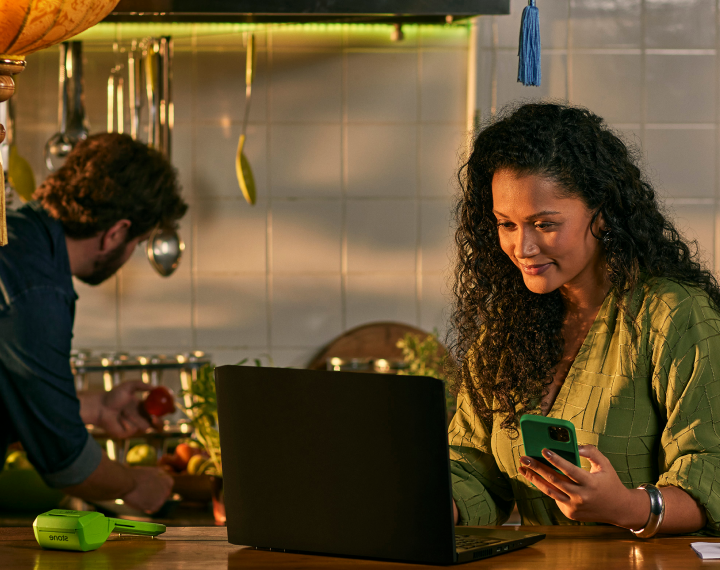 Empreendedora em seu restaurante, utilizando o seu notebook em cima do balcão, ao lado uma Máquina de Cartão da Stone e um celular.