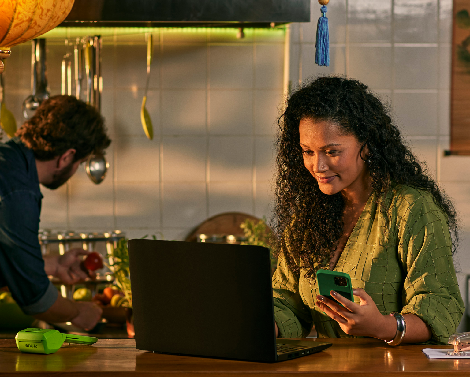 Empreendedora em seu restaurante, utilizando o seu notebook em cima do balcão, ao lado uma Máquina de Cartão da Stone e um celular.
