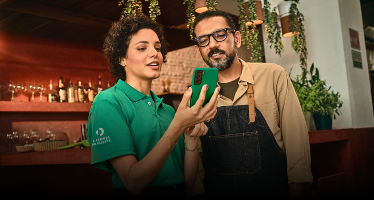 Agente da Stone e cliente interagindo e olhando um celular, representando o suporte presencial da empresa.