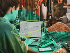 Empreendedora em sua loja mexendo em seu notebook em cima da mesa com a Máquina de Cartão Stone ao lado, celular, lã, e blusa.