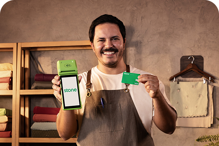 Empreendedor segurando a sua máquina de cartão da Stone e o seu cartão Stone.