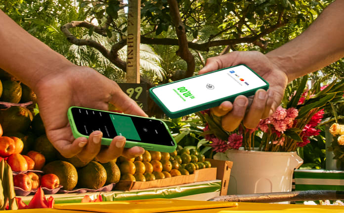 Empreendedor na sua barraca de laranja na feira com o seu celular recebendo o pagamento pelo Tapton, a maquininha no celular por aproximação do seu cliente.