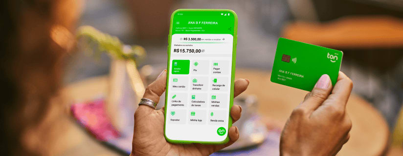Empreendedor segurando na sua mão esquerda o celular com o app do Ton aberto e na mão direita o cartão do Ton