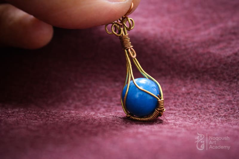 Blue round bead enclosed in a gold wire cage pendant.