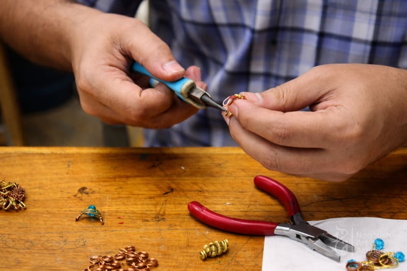 Hands using needle-nose pliers to bend copper wire into a small loop.