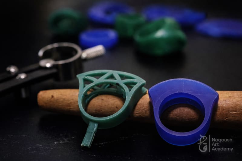 نماذج خواتم شمع (Wax Models) خضراء وزرقاء مع أداة قياس (Calipers) لضبط المقاسات.