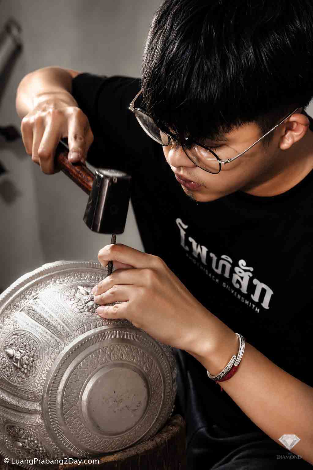A great-grandson of the former Royal Palace silversmith carefully hand-engraves a ceremonial silver bowl inside the Phothisak Rattanakorn workshop in Luang Prabang. A great-grandson of the former Royal Palace silversmith carefully hand-engraves a ceremonial silver bowl inside the Phothisak Rattanakorn workshop in Luang Prabang.