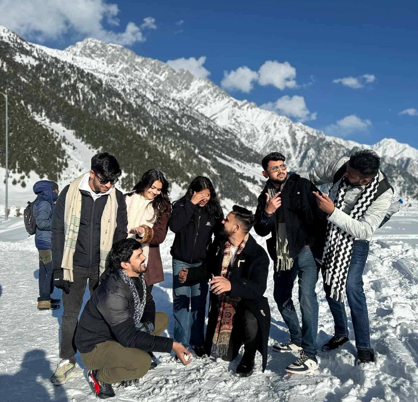 Travellers posing against snow-covered mountains in Kashmir