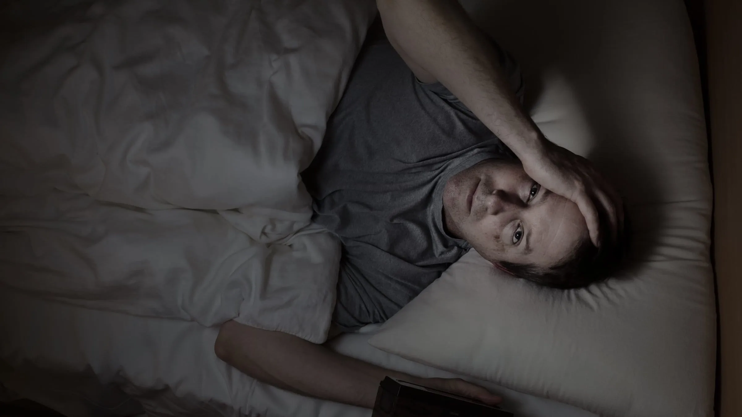A man sitting up in bed with a worried expression, clearly portraying difficulty in staying asleep.