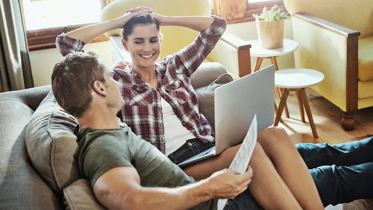 A woman at home looking at financial documents with a laptop, representing financial stress in a relatable everyday setting.