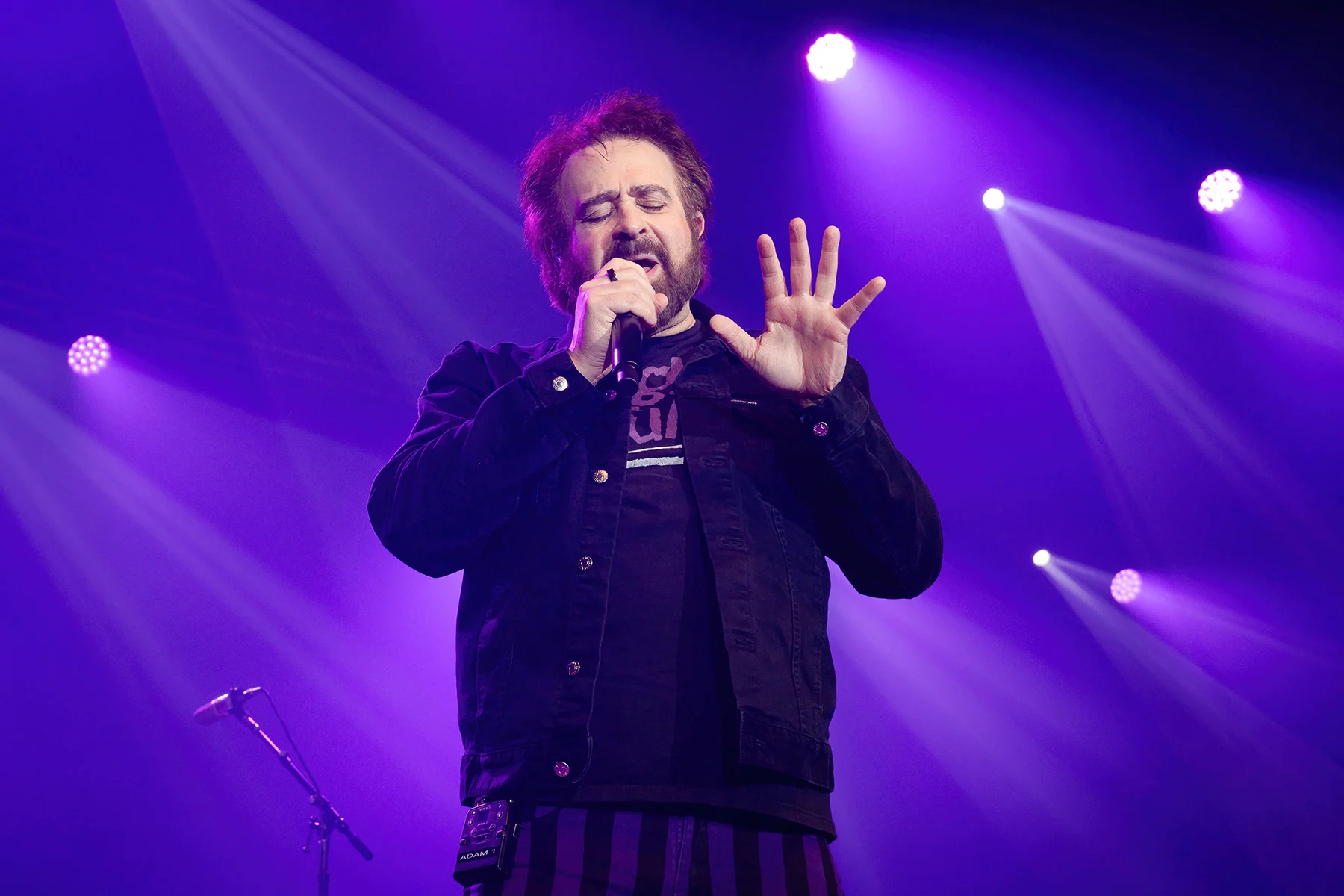 Adam Duritz of Counting Crows performing live in 2025, captured in vibrant stage lighting during the Scleroderma Research Foundation's Cool Comedy • Hot Cuisine event.