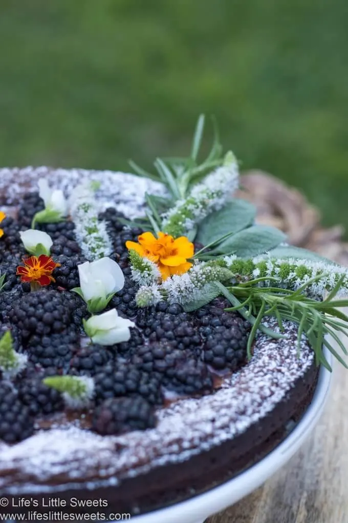 Detailed shot of flourless chocolate cake with blackberries and edible flowers; vertical format and clear focus.