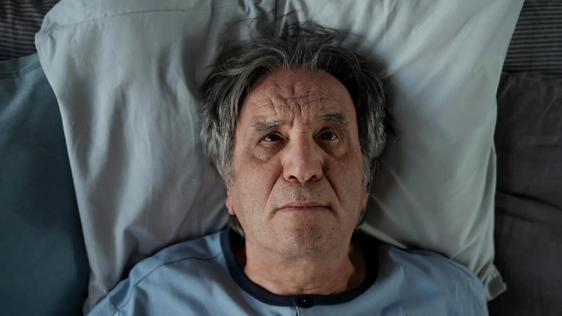 High-quality image of an elderly man lying awake in bed, contextualizing sleep disorders relevant to Alzheimer’s disease.
