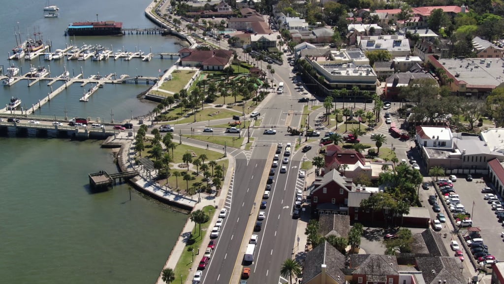 Aerial view of a coastal town with a marina, boats, waterfront park, busy streets, palm trees, and buildings along the shoreline on a sunny day—a perfect snapshot for anyone searching for things to do in Northeast Florida this summer.