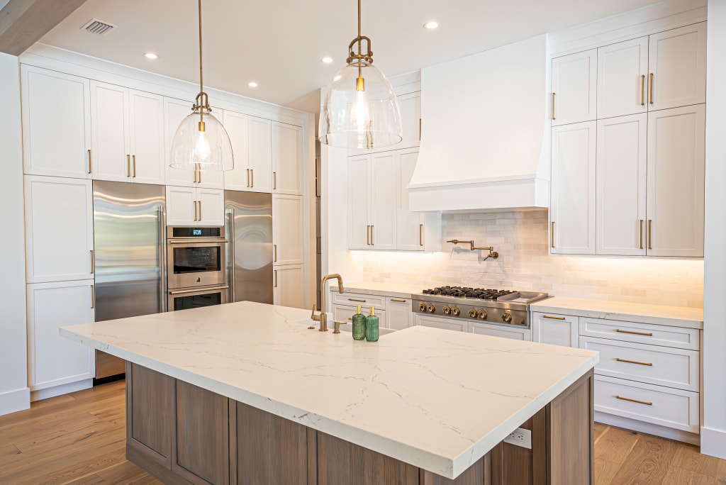 Modern kitchen with white cabinets, stainless steel appliances, marble island, built-in oven, gas stove, wooden floor, and two large glass pendant lights—perfect for luxury homes in Nocatee FL.