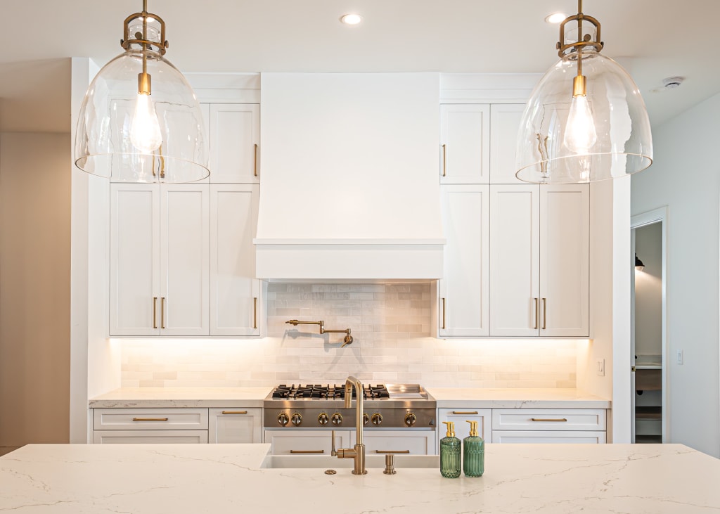 A modern kitchen with white cabinets, marble countertops, a stainless steel stove, two glass pendant lights, and decorative green bottles on the island—a bright, minimalistic space found in many homes in Nocatee FL.