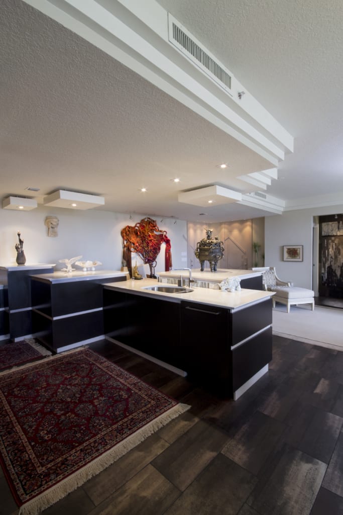 Modern open-concept kitchen with dark cabinets, white countertops, and a patterned rug, featuring contemporary art sculptures and colorful wall art in a bright, spacious living area.
