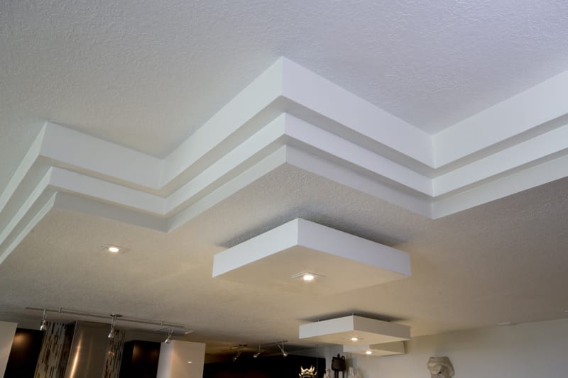 Modern ceiling design with layered, geometric white panels and recessed lighting fixtures, creating a stylish and contemporary look in the room.