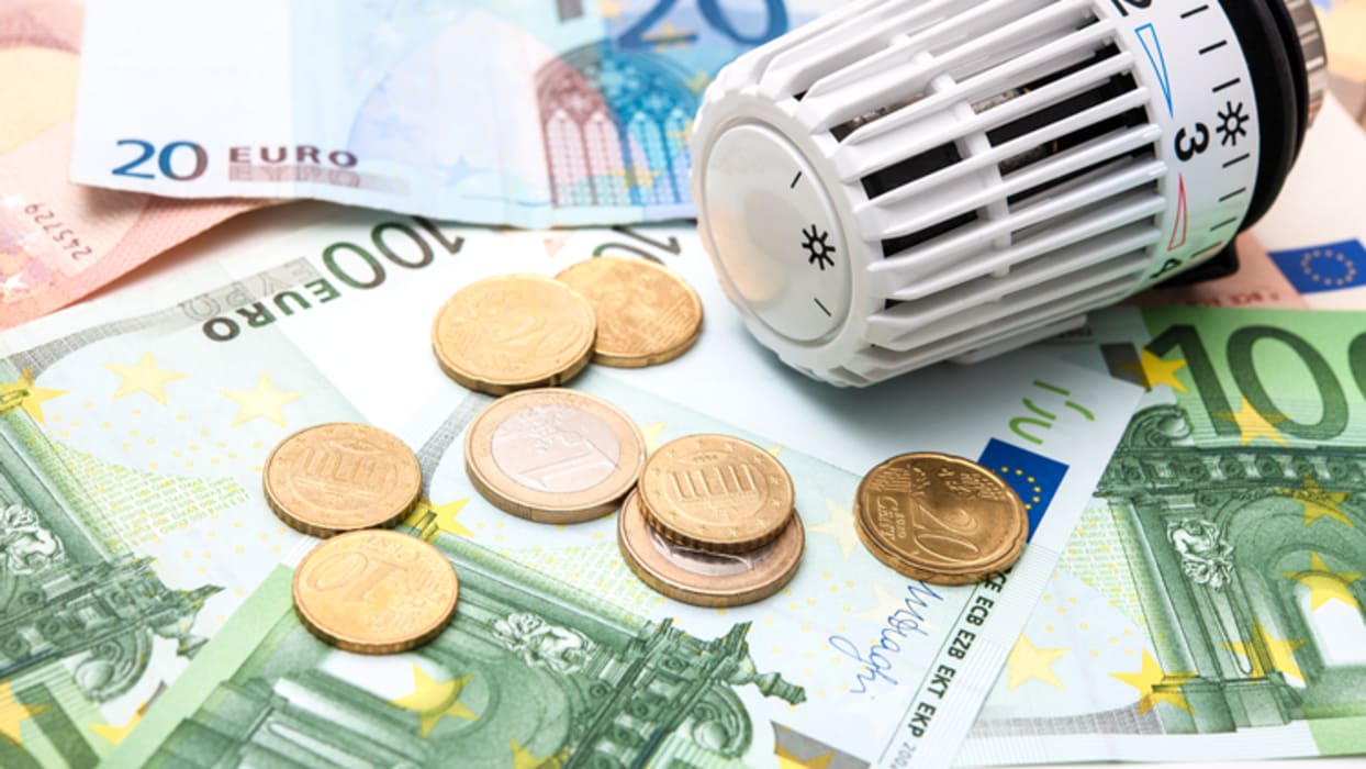 Ein Thermostatkopf liegt auf einem Haufen von Euro-Banknoten und -Münzen.