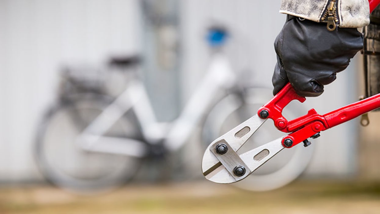Person steht mit Bolzenschneider vor Fahrrad, das durch Haushaltsversicherung gegen Fahrraddiebstahl abgesichert ist. 