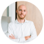 Ein Mann in einem weißen Hemd steht mit verschränkten Armen vor einer hellen Holz- und Glaswand. Sein Gesicht ist unscharf dargestellt. Sein Erscheinungsbild wirkt geschäftlich und professionell.