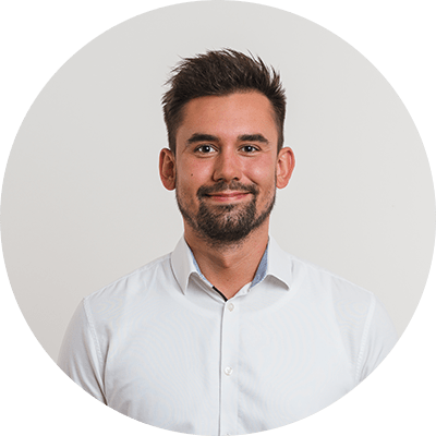 Ein Mann trägt ein weißes Hemd mit einem dezenten blauen Rand am Kragen. Der Hintergrund ist einfarbig hellgrau, und das Bild ist kreisförmig ausgeschnitten.