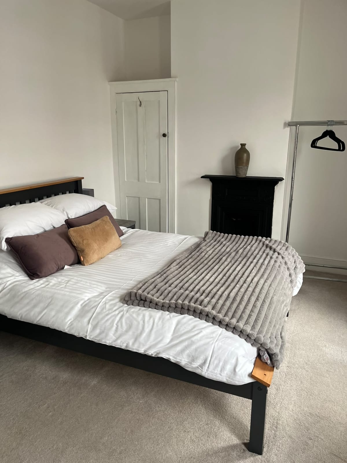 Double bed with white bedding, mauve cushions, gray throw, and fireplace