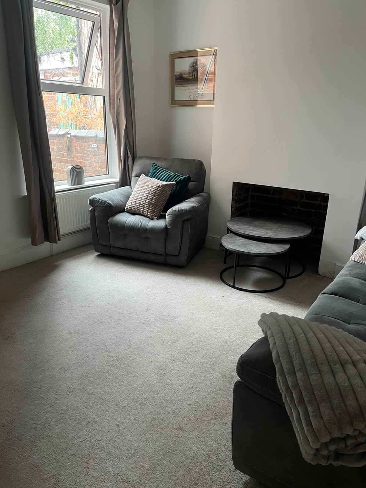 Living room alcove with gray armchair, brick fireplace recess, and nesting tables