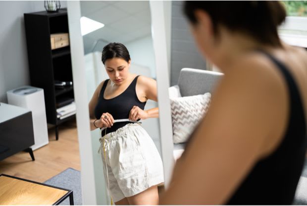 a woman measuring her waist in front of a mirror