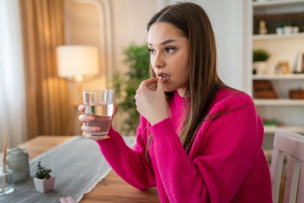A woman taking a pill with a glass of water