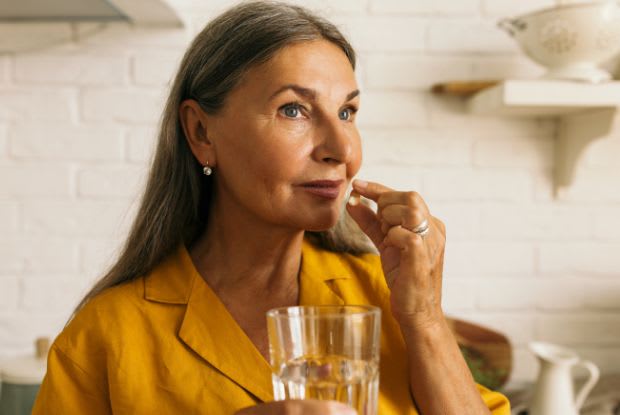 An elderly woman taking a tablet with a glass of water