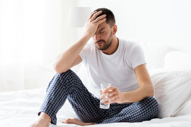 a man with a headache sitting in bed with a glass of water
