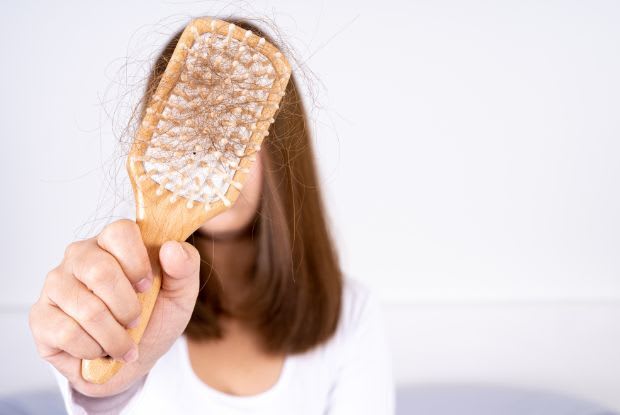 A woman holding up a hairbrush with hair strands