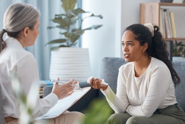 A sad woman holding a tissue and talking to a therapist